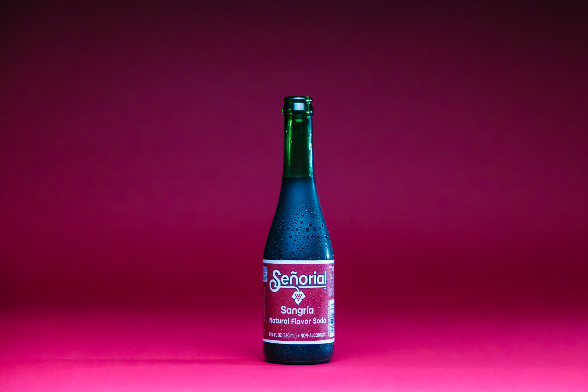  A single beer bottle with a vibrant label placed against a pink background