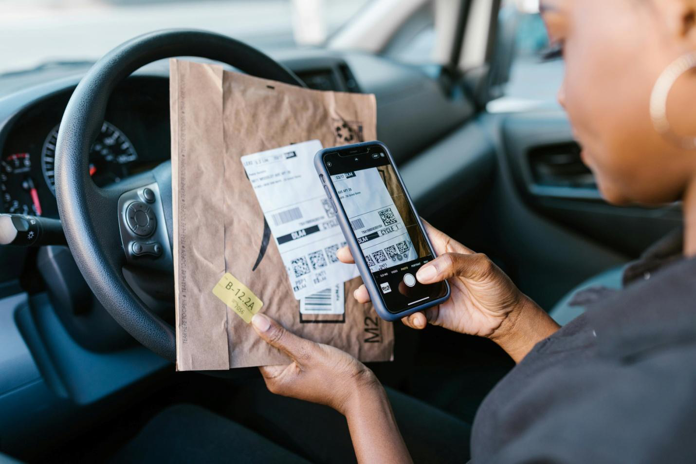 a woman scanning a barcode on a brown packaged parcel inside a car